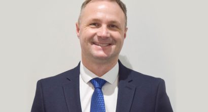 Man (R Harding) in suit in front of white wall smiling at camera